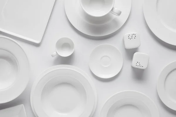 Vue du dessus de différentes assiettes, bol, salière, poivrière et tasse sur table blanche — Photo de stock