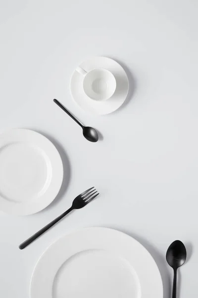 Vista superior de platos, taza, tenedor y cucharas negras sobre mesa blanca — Stock Photo