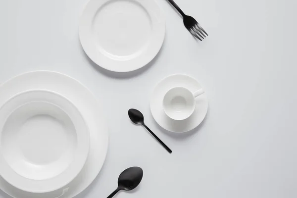 Top view of various plates, cup, black spoons and fork on white table — Stock Photo