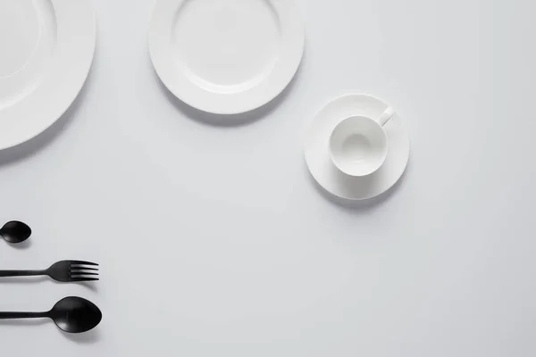 Вид сверху на разные тарелки, чашки, черные ложки и вилку на белый стол — стоковое фото