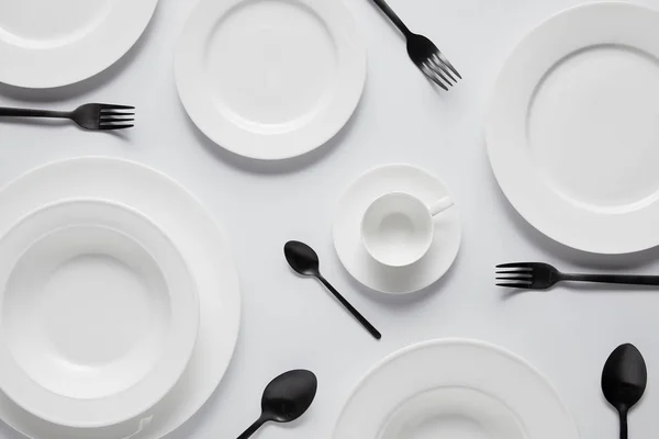 Top view of various plates, cup, black spoons and forks on white table — Stock Photo