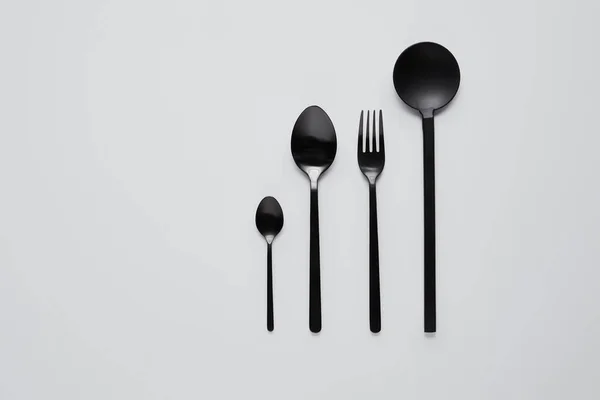 Vue de dessus de différentes cuillères noires, fourchette et cuillère à salade sur table blanche, concept minimaliste — Photo de stock