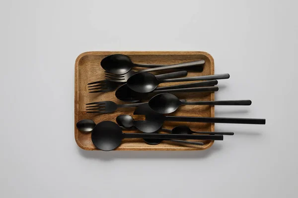 Vista dall'alto del vassoio in legno con vari cucchiai, forchette e cucchiaio da insalata sul tavolo bianco — Foto stock