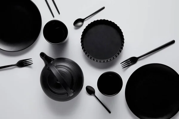 Vue de dessus de théière noire, assiettes, plat de cuisson, tasses, cuillères, baguettes et fourchettes sur table blanche — Photo de stock