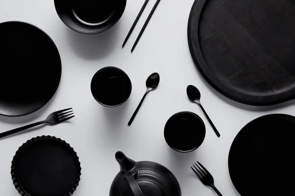 Top view of black teapot, spoons, forks, chopsticks, cups, tray, bowl, plates and baking dish on white table — Stock Photo