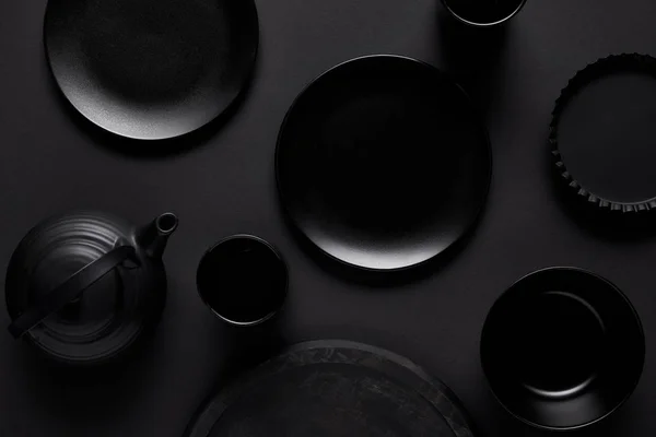 Top view of black teapot, plates, bowl, cups, tray and baking dish on black table — Stock Photo