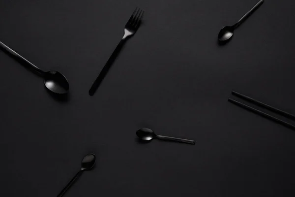 Vista superior de varias cucharas negras, tenedor y palillos en la mesa negra - foto de stock