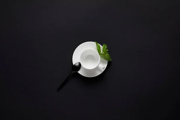 Vue du dessus de la tasse vide, cuillère noire et feuilles de menthe sur table noire — Photo de stock