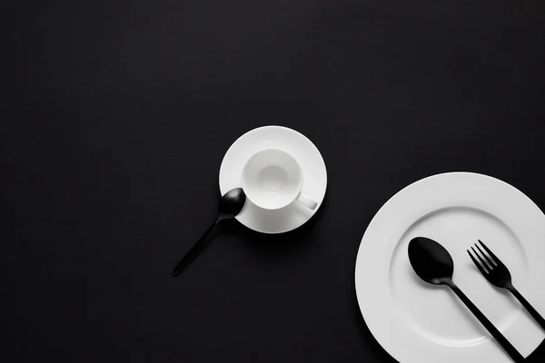 Top view of plate, cup, black spoons and fork on black table — Stock Photo