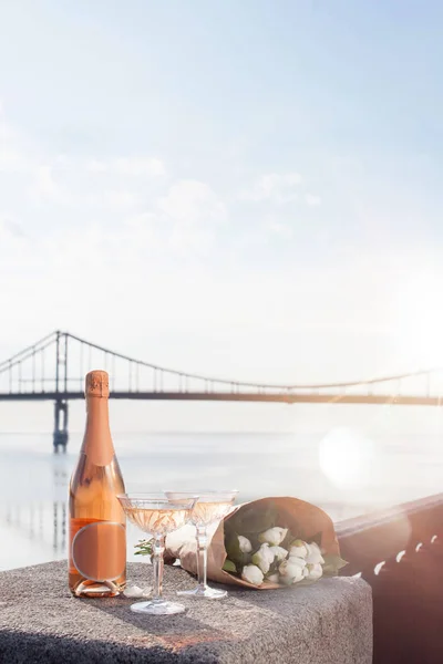 Close-up view of beautiful bouquet of flowers, glasses and bottle of champagne at riverside — Stock Photo