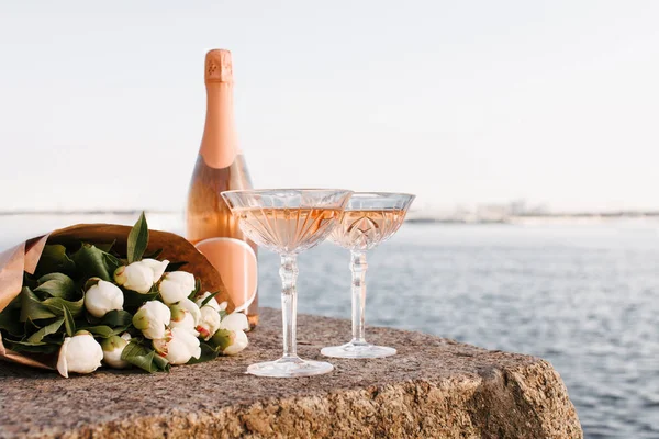 Close-up view of two glasses, bottle of champagne and beautiful bouquet of flowers on embankment at riverside — Stock Photo