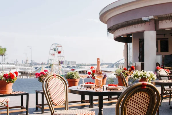 Bottle of champagne, glasses and gourmet desserts on round table in outdoor cafe — Stock Photo