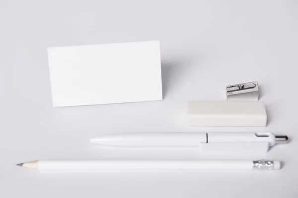 Primer plano de la tarjeta de visita y la pluma con lápiz, goma de borrar y sacapuntas dispuestos en fila en la superficie blanca para maqueta - foto de stock