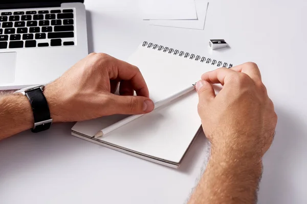 Cropped shot of man with notepad and pencil lying at workplace on white surface — Stock Photo