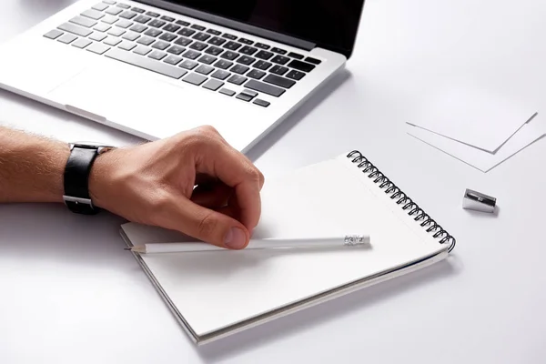 Ritagliato colpo di uomo con notebook e matita sdraiato sul posto di lavoro su superficie bianca — Foto stock