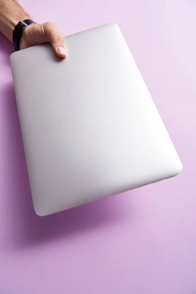 Обрезанный снимок человека, держащего сложенный ноутбук над розовой поверхностью — стоковое фото
