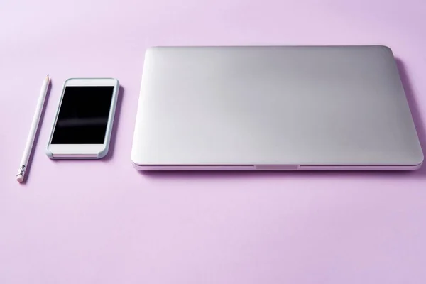 Primer plano de la computadora portátil con teléfono inteligente en la superficie rosa - foto de stock