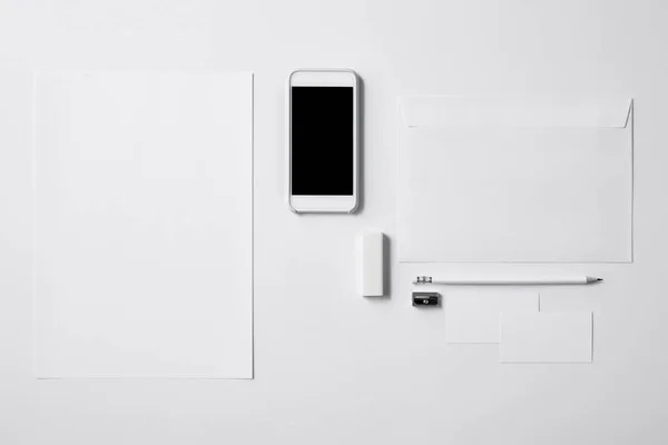 Vista dall'alto dello smartphone con schermo bianco e forniture da ufficio su tavolo bianco per il mockup — Foto stock