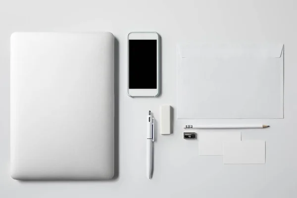 Vista dall'alto del computer portatile con smartphone e forniture da ufficio su tavolo bianco per il mockup — Foto stock