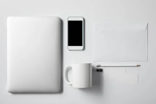 Верхний вид ноутбука со смартфоном, чашкой и офисными принадлежностями на белом столе для макета — стоковое фото