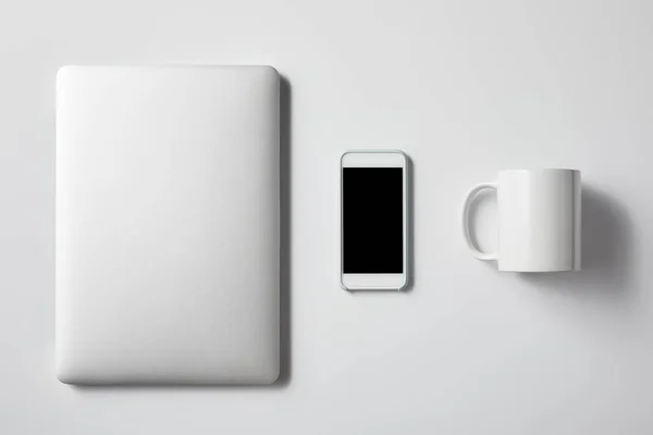 Ansicht von Laptop mit Smartphone und Tasse auf weißer Tischplatte für Attrappe — Stockfoto