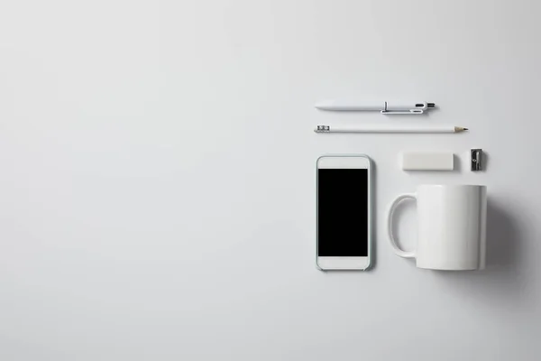 Vue de dessus du smartphone avec diverses fournitures et tasse sur la surface blanche pour la maquette — Photo de stock