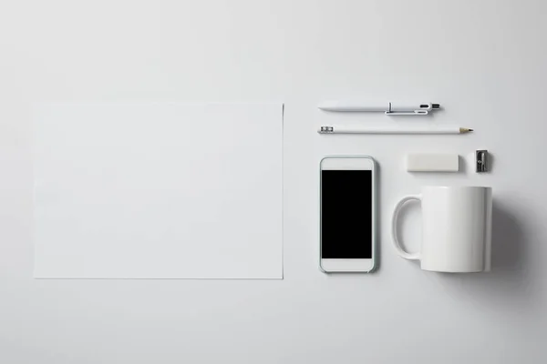 Vista superior do smartphone com vários suprimentos e papel em branco na mesa branca para mockup — Fotografia de Stock