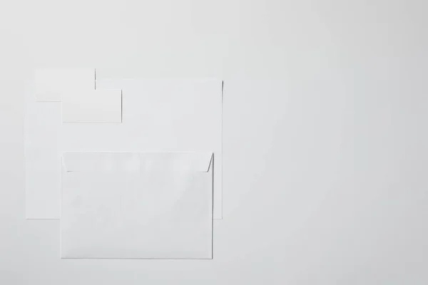 Vista superior de papel en blanco con sobre y tarjetas de visita en la superficie blanca para maqueta - foto de stock