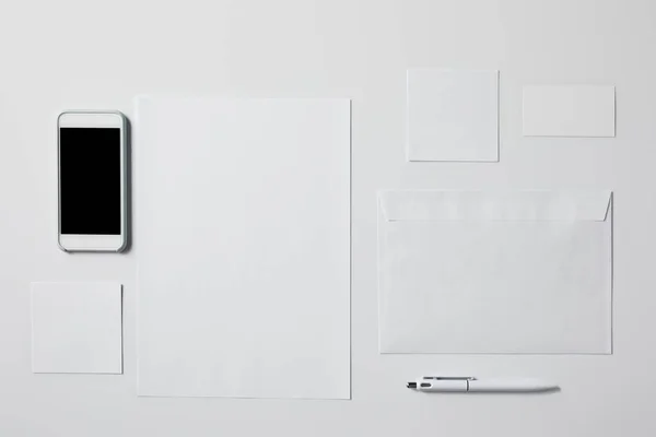 Вид зверху смартфона з різними порожніми паперами і ручкою на білому столі для маскування — стокове фото