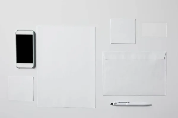 Vue du haut du smartphone avec divers papiers vierges et stylo sur la table blanche pour la maquette — Photo de stock