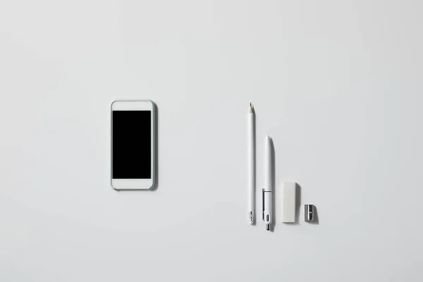 Вид сверху на смартфон с различными расходными материалами подряд на белом столе для макета — стоковое фото