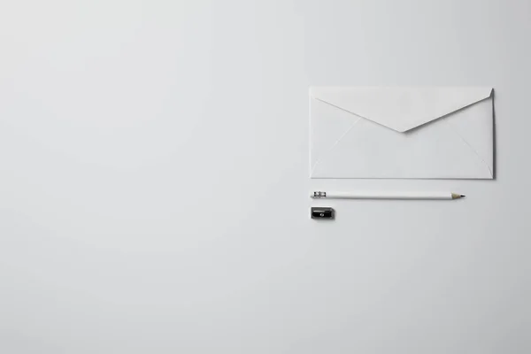 Верхний вид конверта с карандашом и точилкой на белой поверхности для макета — стоковое фото