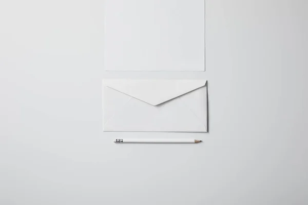 Top view of envelope with blank paper and pencil on white surface for mockup — Stock Photo