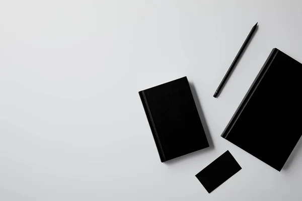 Vista superior de cadernos pretos com cartão de visita e lápis na mesa branca para maquete — Fotografia de Stock
