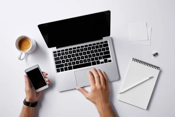 Abgeschnittene Aufnahme eines Mannes, der mit Laptop arbeitet und Smartphone in der Hand auf weißer Oberfläche zum Attrappen hält — Stockfoto