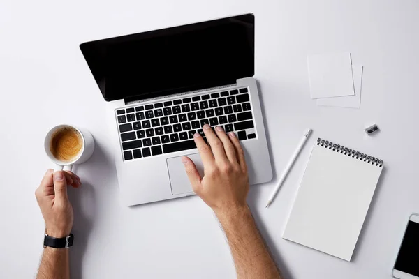 Tiro cortado do homem que trabalha com laptop e tendo xícara de café no local de trabalho na superfície branca para maquete — Fotografia de Stock