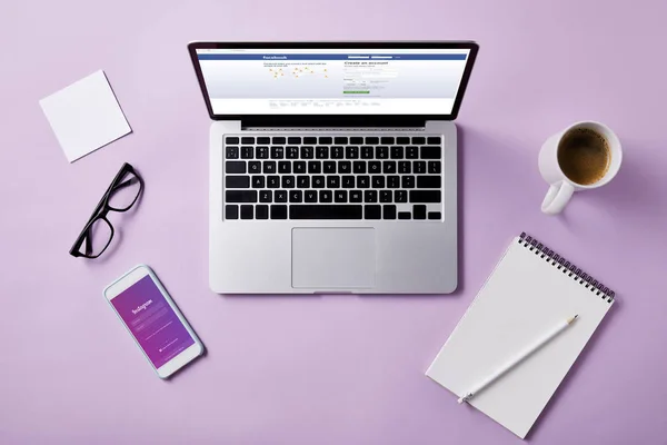 Top view of laptop with facebook website on screen and smartphone with instagram app on pink tabletop for mockup — Stock Photo