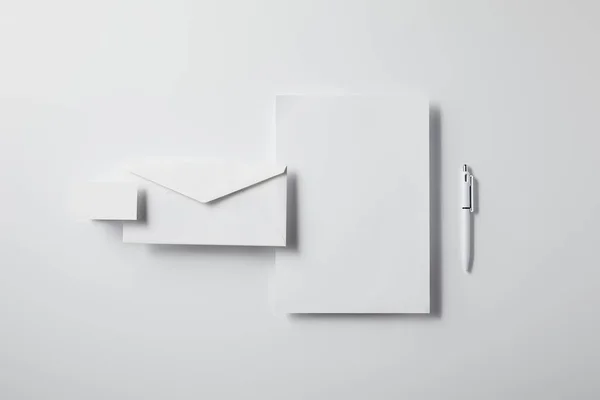 Top view of layered envelope with pen, blank paper and business card on white tabletop for mockup — Stock Photo