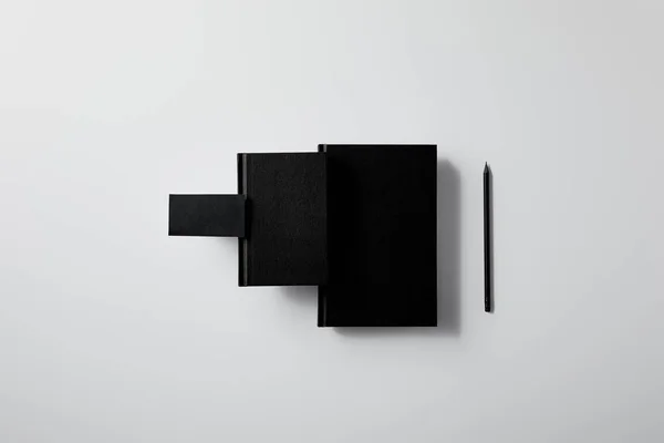 Vue du dessus des carnets noirs avec carte de visite et crayon en rangée sur la surface blanche pour la maquette — Photo de stock