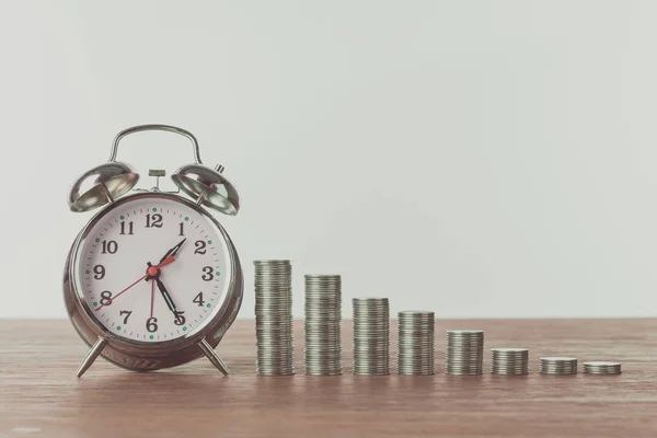 Alarm clock and stacks of coins on wooden table, saving concept — Stock Photo