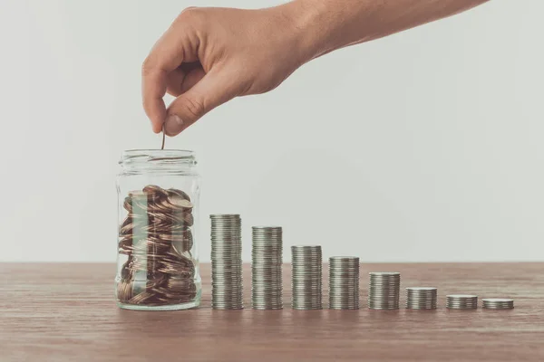 Cropped image of man putting coin into jar on wooden table, saving concept — Stock Photo