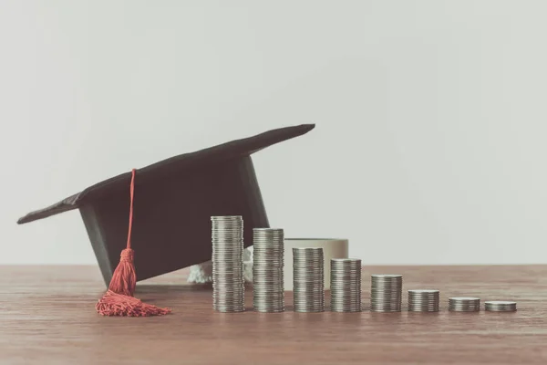 Stacks of coins and graduation cap on wooden table, saving concept — Stock Photo