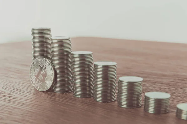 Un Bitcoin près des piles de pièces sur une table en bois, concept d'économie — Photo de stock