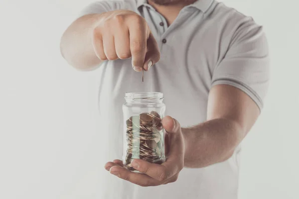 Imagen recortada del hombre poniendo moneda en tarro aislado en blanco, ahorrando concepto - foto de stock