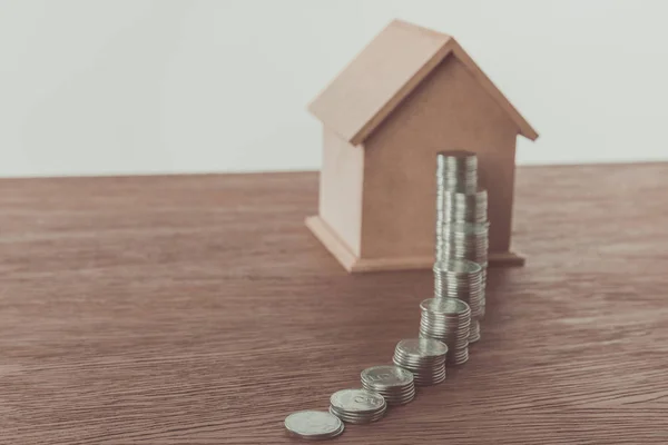 Pilhas de moedas e pequena casa de madeira na mesa marrom, economizando conceito — Fotografia de Stock