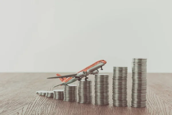 Avião de brinquedo em pilhas de moedas na mesa de madeira, economizando conceito — Fotografia de Stock