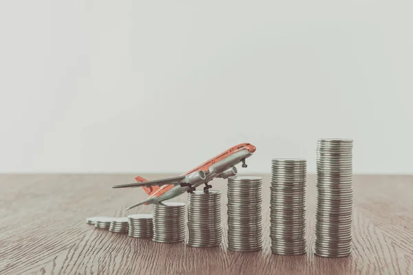 Toy plane on stacks of coins on wooden table, saving concept — Stock Photo