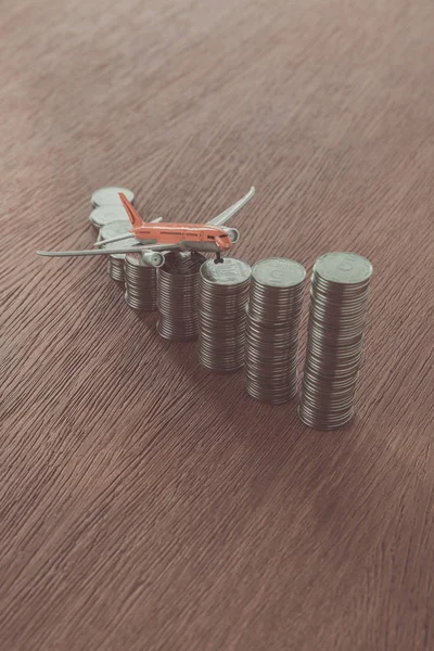 Avião de brinquedo em pilhas de moedas em mesa de madeira, economizando conceito — Fotografia de Stock
