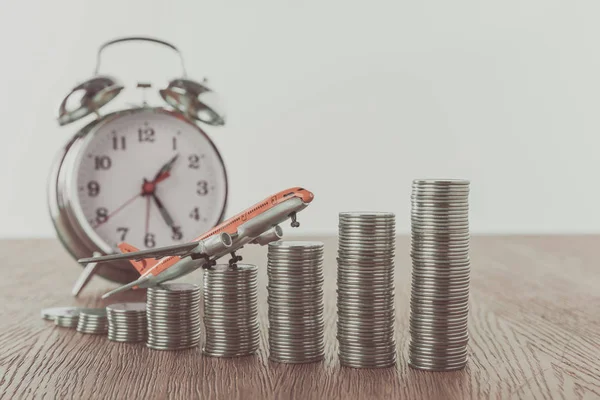 Toy plane on stacks of coins and alarm clock on wooden table, saving concept — Stock Photo