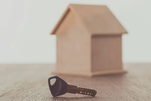 Chave e pequena casa na mesa de madeira, economizando conceito — Fotografia de Stock